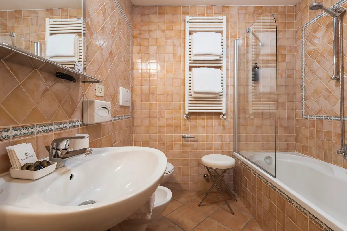Bagno della Family Room in stile classico, con vasca, lavabo e piastrelle color terra a Cortina d'Ampezzo. | Classic-style family room bathroom with bathtub, sink, and warm-toned tiles in Cortina d'Ampezzo.
