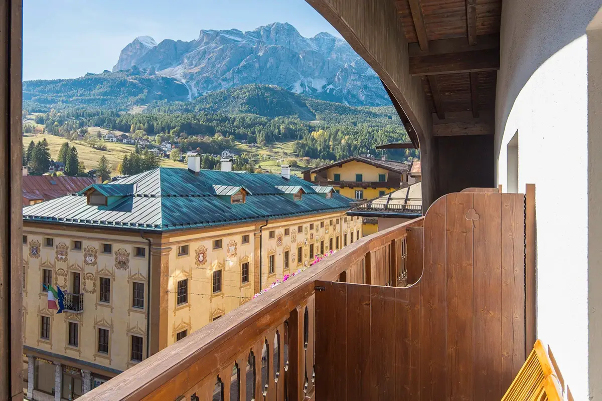 Balcone panoramico della Family Room con vista sulle Dolomiti e sedie in legno. | Panoramic Family Room balcony with Dolomites mountain view and wooden chairs.