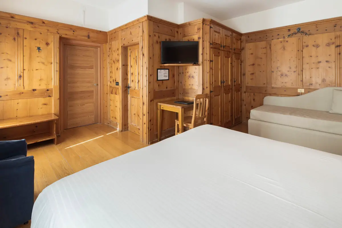 Camera Superior Tripla in legno cirmolo con angolo relax – Hotel Montana Cortina. | Superior Triple Room with Swiss pine wood and relaxation corner – Hotel Montana Cortina.