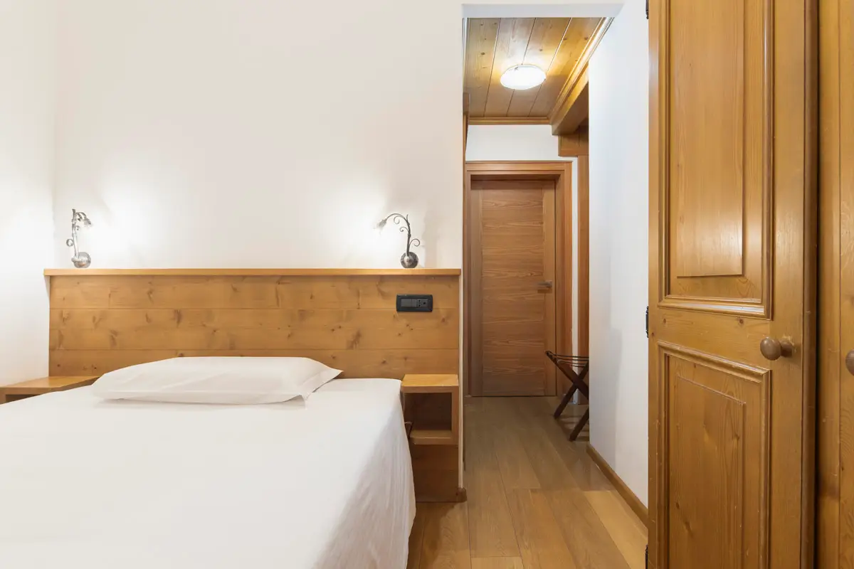 Camera Singola Superior con design caldo e parete in legno alpino. | Single Superior room with warm design and alpine wood paneling.