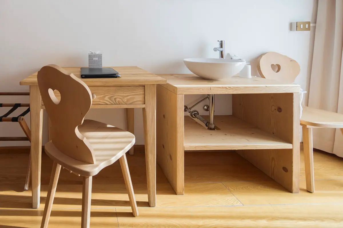 Dettaglio della scrivania in legno e del lavandino nella Family Room, design tradizionale ampezzano. | Detail of wooden desk and sink in the Family Room, traditional Ampezzo-style design.
