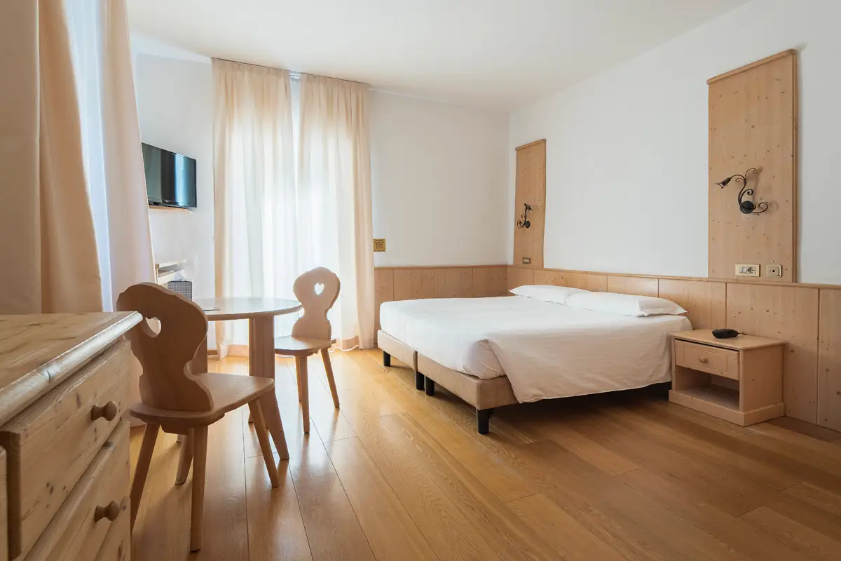 Seconda stanza della Family Suite, ampia e luminosa, con arredamento in legno e vista esterna. | Second bedroom of the Family Suite, spacious and bright, with wooden furniture and exterior view.