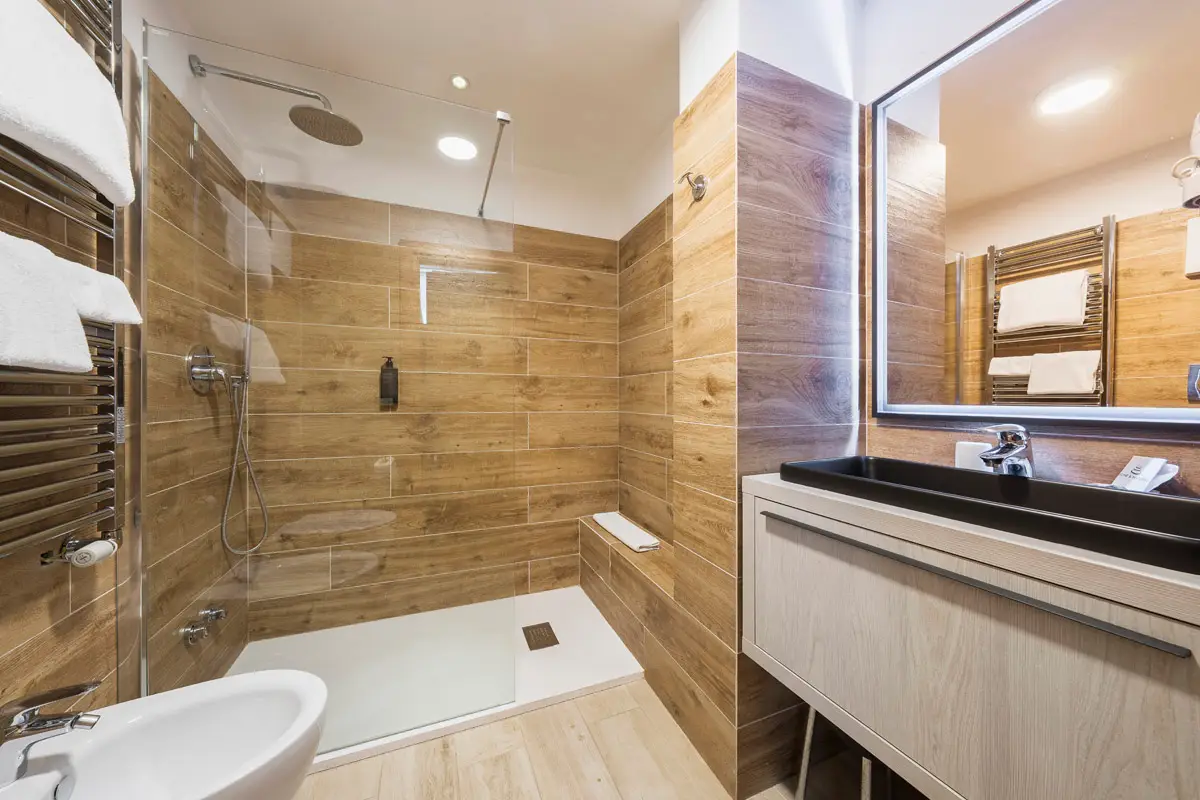 Bagno Singola Superior con doccia walk-in e rivestimento effetto legno. | Single Superior bathroom with walk-in shower and wood-effect tiles.